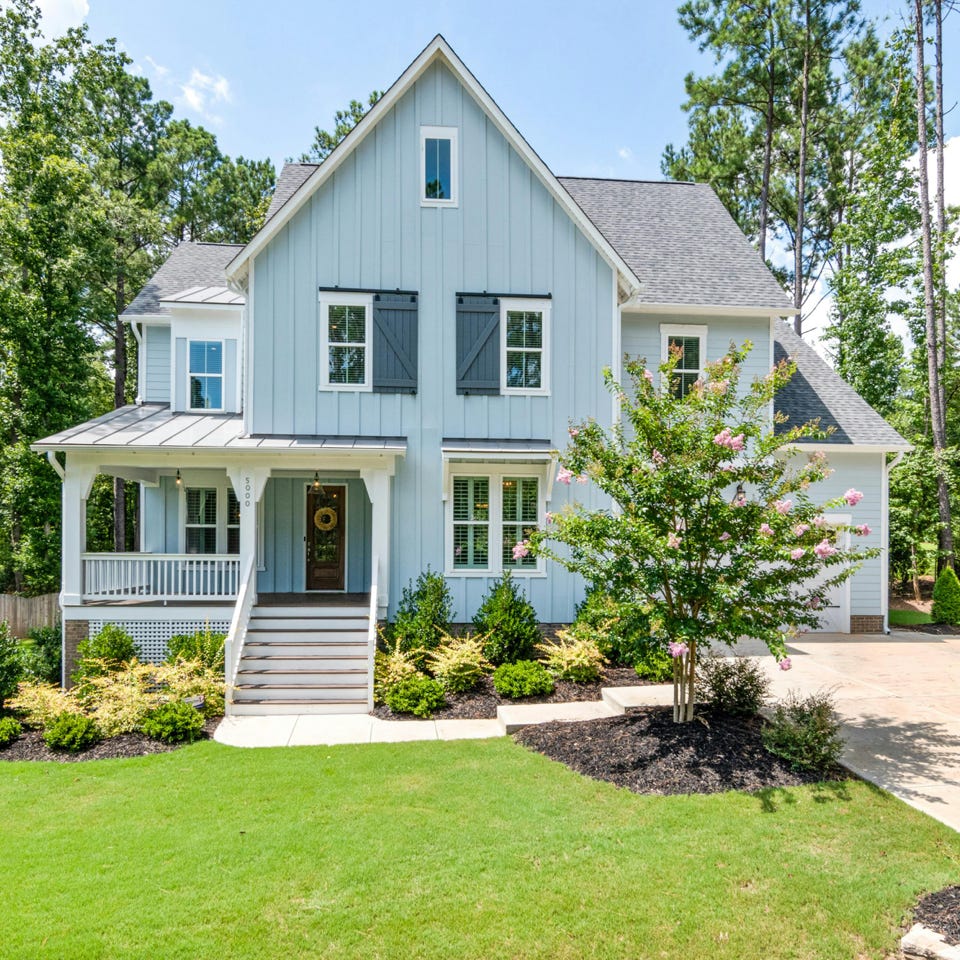 Person washing a car with a hose outdoors, creating suds on a sunny day.